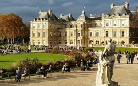 Palacio de Luxemburgo y su jardín con gente sentada y un monumento.