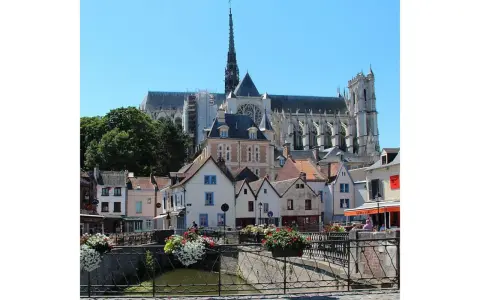 Blick auf malerische Häuser und die Kathedrale in Amiens, Frankreich. Blumenkästen schmücken eine Brücke über einen Kanal.