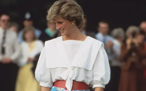 Lady Di sonríe con un conjunto blanco y rojo, un ejemplo de sus icónicos outfits.