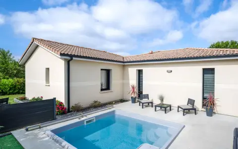 Vue aérienne d'une maison moderne avec piscine, le **plan maison en L** est bien visible, entouré de verdure.