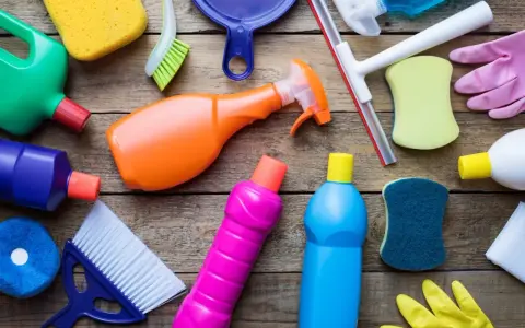 Divers produits et accessoires de nettoyage colorés sur fond de bois.