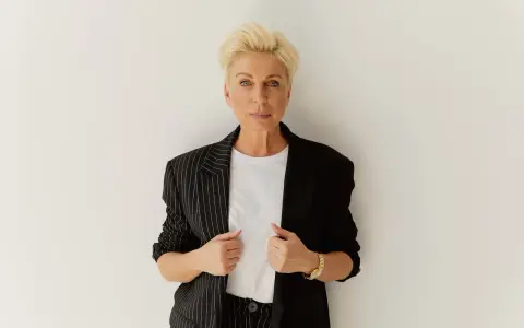 Elegancka kobieta z blond włosami, w czarnej marynarce w paski, pokazuje, jak powinna leżeć marynarka, podkreślając jej stylowy krój.