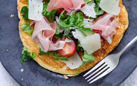 Pyszny przepis na omlet na słono z szynką parmeńską, parmezanem, pomidorkami i rukolą. Idealny na szybki obiad lub kolację.