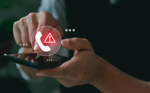 Mano sosteniendo un teléfono con un icono de llamada y advertencia.