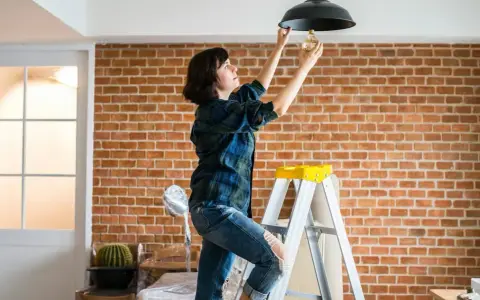 Une femme sur une échelle change une ampoule. L'indemnisation assurance obligation faire travaux est en cours.