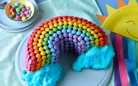 Bunter regenbogen kuchen, verziert mit vielen bunten Smarties und blauer Zuckerwatte als Wolken. Ein Fest für die Augen!