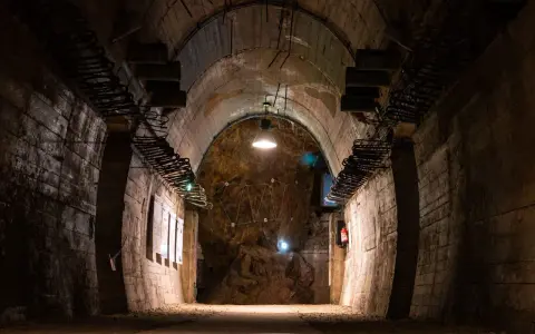 Wnętrze tunelu w Górach Sowich. Betonowe ściany, łukowe sklepienie i skalna grota z instalacją świetlną.