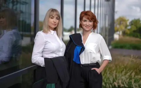 Dwie prawniczki w togach przed nowoczesnym budynkiem.