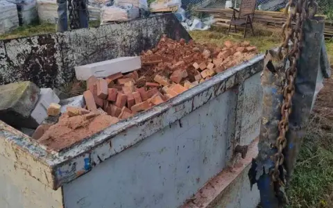 Kontener budowlany z gruzem, cegłami i betonem. W tle widać stosy materiałów budowlanych. Numer referencyjny: 170203.
