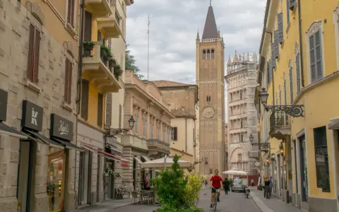 A man cycles down a street in Parma, Italy, with a tall clock tower in the background. This view captures the essence of a journey from Bologna to Parma.