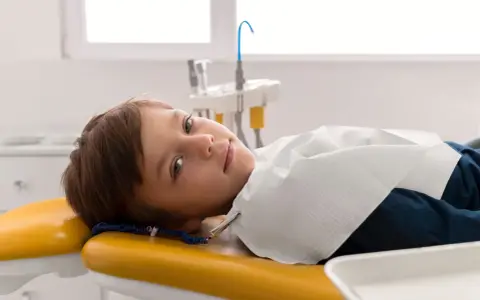 Chłopiec leży na żółtym fotelu dentystycznym, przygotowany do leczenia zębów pod narkozą.
