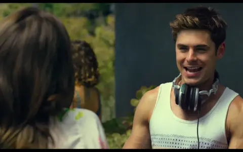 Il cast di We Are Your Friends, Zac Efron con le cuffie al collo, sorride mentre parla con qualcuno fuori campo.