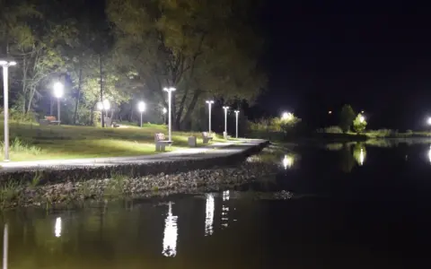 Nocny spacer nad zalewem Wolbromskim. Latarnie oświetlają ścieżkę i ławki, odbijając się w spokojnej tafli wody.