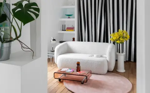 Sofá blanco texturizado, mesa de centro rosa, alfombra redonda y plantas, ideal para una reforma de piso pequeño.