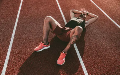 Atleta esausto sdraiato su una pista da corsa, con le mani sulla testa, forse vittima della sindrome da overtraining.