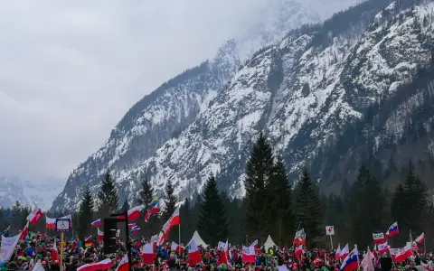 Tłum kibiców z flagami na tle ośnieżonej góry, atmosfera na skoczni w Planicy.