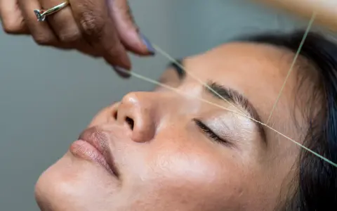 Une main utilise un fil pour épiler ses sourcils.