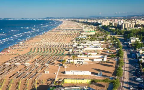 La riviera romagnola dove andare: una distesa infinita di ombrelloni e lettini sulla sabbia dorata, con il mare azzurro e la città sullo sfondo.