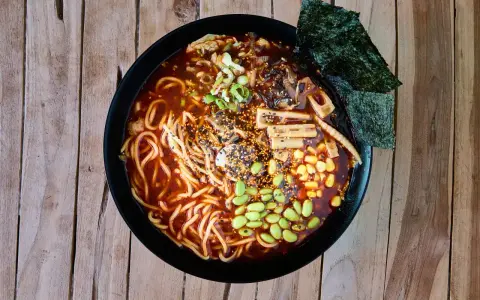 Miseczka aromatycznych dań z makaronem ramen, pełna edamame, kukurydzy, grzybów i nori, na drewnianym tle.