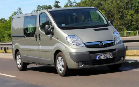 Srebrny Opel Vivaro 2.0 CDTI z przyciemnianymi szybami jedzie po drodze, otoczony zielenią.
