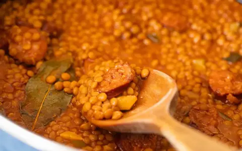 Primer plano de lentejas con chorizo y laurel en una cuchara de madera.