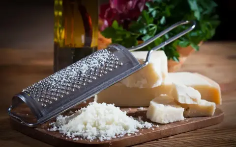 Tarka z kawałkami sera **padano ser** i świeżo startym serem. Obok butelka oliwy i zielenina.