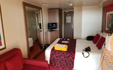 Cabina MSC Musica con letto, divano rosso, specchio e TV. Perfetta per una vacanza in crociera.