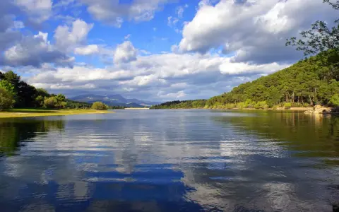 El embalse La Jarosa, con su agua serena reflejando el cielo nublado y rodeado de verdes colinas, invita a la calma.