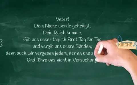 Kreidetafel mit Teilen des Vaterunsers. Eine Hand schreibt "Vater! Dein Name werde geheiligt. Dein Reich komme. Gib uns unser täglich Brot Tag für Tag und vergib uns unsre Sünden; denn auch wir vergeben jedem, der an uns s Und führe uns nicht in Versuc...