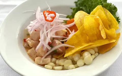 Delicioso ceviche peruano con trozos de pescado fresco, cebolla morada, chile, maíz tierno y chips de plátano.