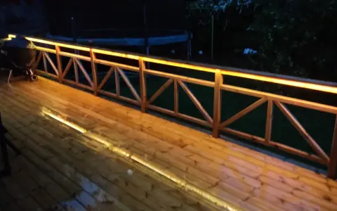 Träaltan med staket upplyst av varma decklights. En grill står på altanen.