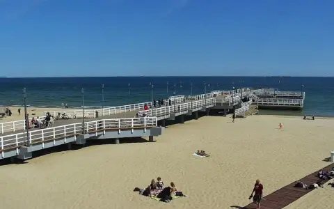 Słoneczny dzień na gdańskiej plaży Brzeźno. Ludzie spacerują po molo, odpoczywają na piasku, ciesząc się widokiem morza.