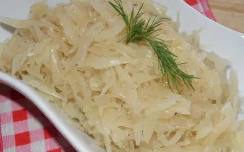 Gotowana biała kapusta do obiadu, podana w białej misce, ozdobiona gałązką koperku.