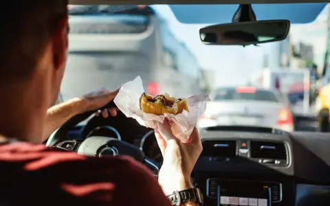 Uomo al volante mangia un panino in un ingorgo. Si può mangiare mentre si guida, ma attenzione alla sicurezza!