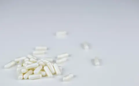 Białe kapsułki leżą na białym tle. To suplementy, które mogą pomóc w walce z bólem, podobnie jak anapran na co jest.