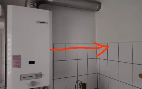Ein Junkers-Durchlauferhitzer mit Gasflasche ist an der Wand montiert. Ein roter Pfeil zeigt auf die Ecke.