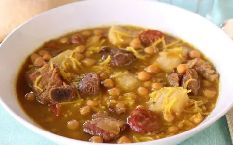 Un reconfortante rancho canario en un cuenco blanco, con garbanzos, trozos de carne, patatas y fideos finos.