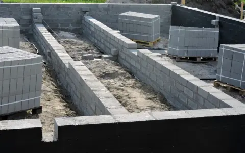 Fundament budowy z bloczków betonowych, przygotowany pod izolację przeciwwilgociową. Materiały budowlane czekają na użycie.