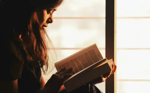 Ragazza immersa nella lettura, illuminata dalla luce dorata del tramonto, sfoglia pagine che potrebbero contenere i libri di Emmanuel Carrère.