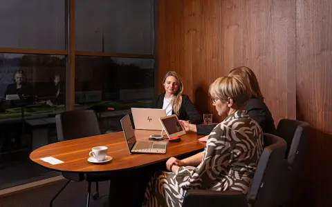 Trzy kobiety omawiają strategię w nowoczesnym biurze. Dyskretne spotkanie, które może dotyczyć usług private banking.