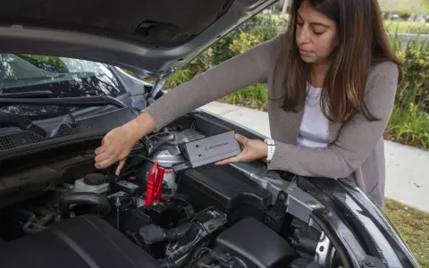 Woman connects a jump starter to a car battery. She's learning how to reset my jump starter.