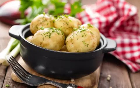 Gotujesz ziemniaki na ból ucha? Te młode ziemniaczki, posypane koperkiem, wyglądają apetycznie. Obok widelec i czerwono-biała serwetka.