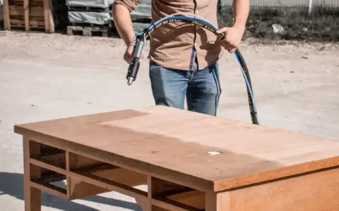 Un homme utilise un appareil pour poncer ou décaper un bureau en bois, révélant une surface plus claire.
