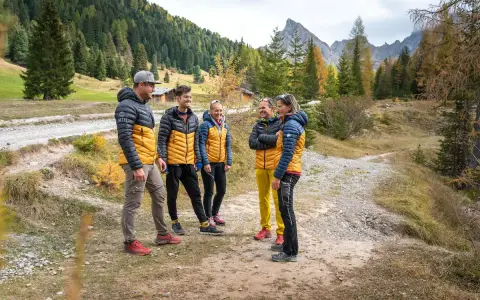 Gruppo di escursionisti con giacche imbottite gialle e blu, pantaloni tecnici e scarponi. Perfetto esempio di come vestirsi in montagna per un'avventura autunnale.