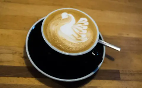 Cappuccino mit Milch-Schwan-Latte-Art auf schwarzer Untertasse. Perfekt für jeden Kaffeeliebhaber.