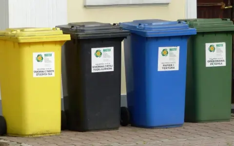 Cztery kolorowe kosze na śmieci: żółty na folię, czarny na metale, niebieski na papier i zielony na szkło. Różne rodzaje koszy ułatwiają segregację.