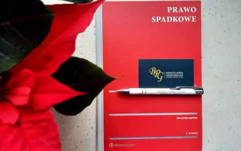 Czerwona książka "Prawo spadkowe" obok poinsecji. Długopis z nazwiskiem adwokatki i wizytówka kancelarii sugerują tematykę prawną, być może związaną z zapisem windykacyjnym.