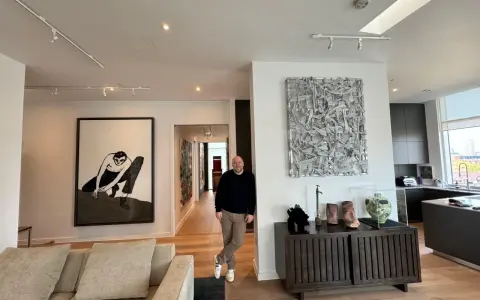 Guy Hepner stands in a modern apartment filled with art, including a large black and white drawing and a textured sculpture.