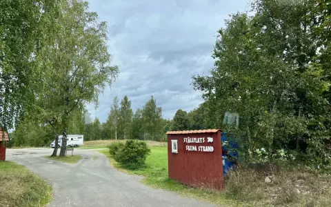 Välkommen till ställplatsen vid Skeda strand. En husbil står parkerad bland träden.