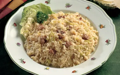 Un saporito risotto con verza e salsiccia, guarnito con una foglia di verza fresca e un ciuffo di prezzemolo.